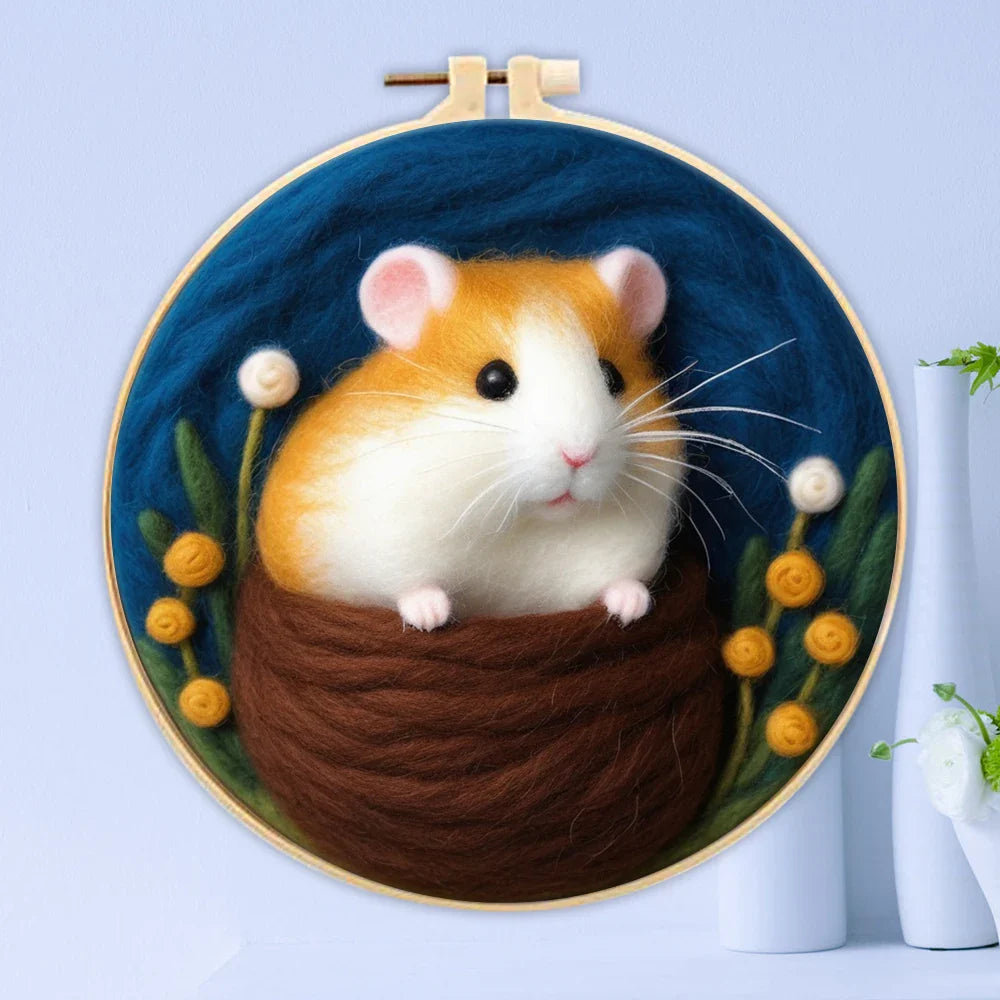 A person's hands holding a DIY felting kit with a pre-printed felt cloth depicting a white cat with orange spots, surrounded by colorful wool in the background.