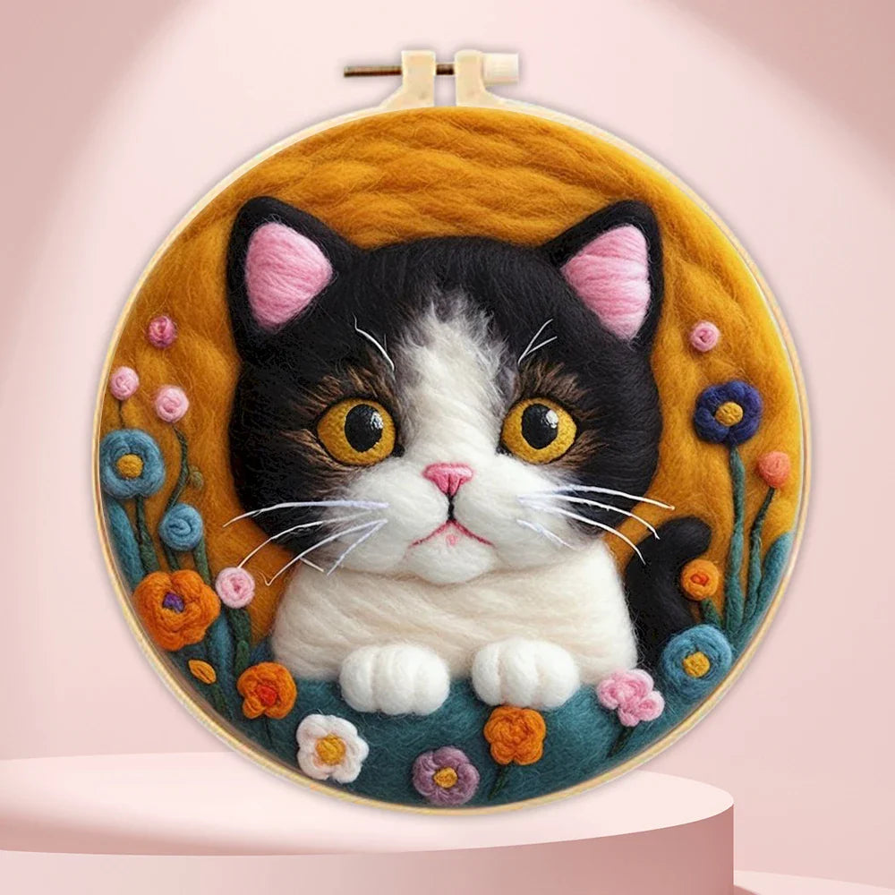 A person's hands holding a DIY felting kit with a pre-printed felt cloth depicting a white cat with orange spots, surrounded by colorful wool in the background.