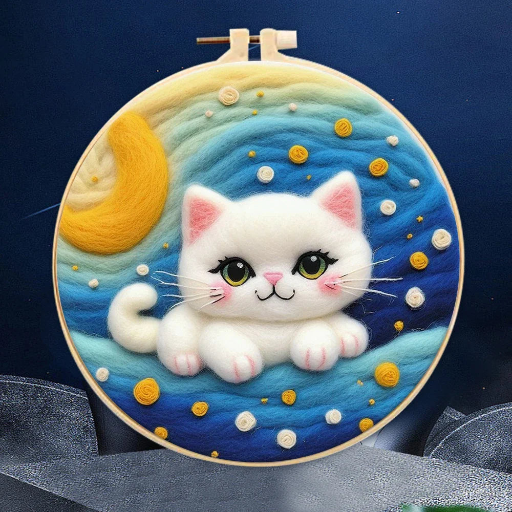 A person's hands holding a DIY felting kit with a pre-printed felt cloth depicting a white cat with orange spots, surrounded by colorful wool in the background.