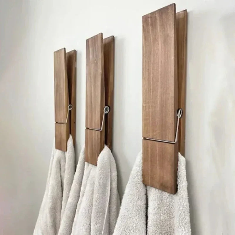 A large wooden clothespin mounted on a wall holding a grey towel.