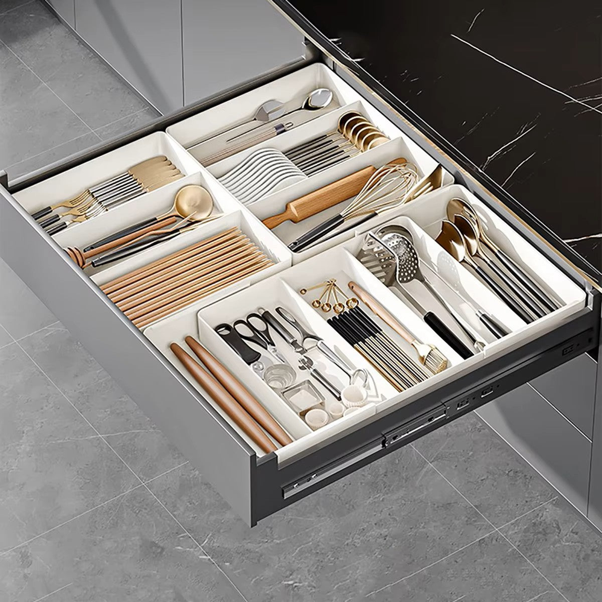 Extendable drawer organizer with various compartments filled with cutlery and kitchen utensils, fitted in an open drawer.