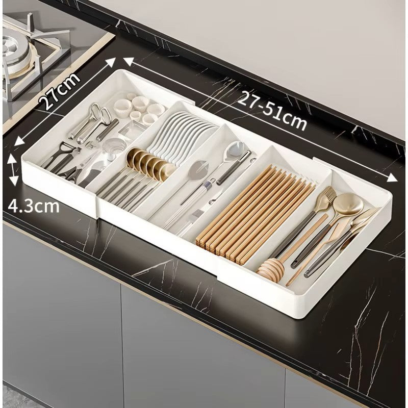 Extendable drawer organizer with various compartments filled with cutlery and kitchen utensils, fitted in an open drawer.