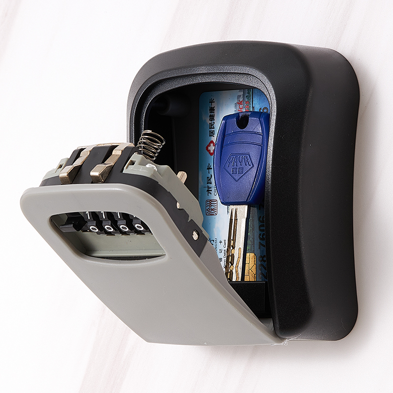 A wall-mounted key safe with a combination lock, in a gray color, partially open to show the keys inside.
