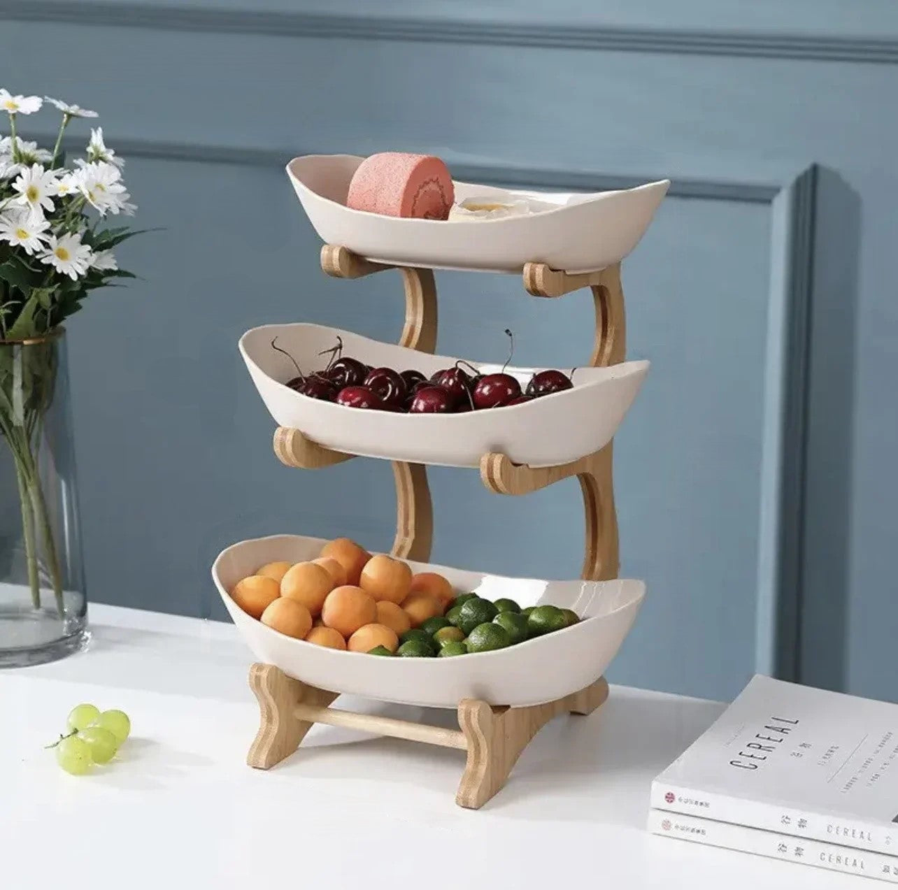 A set of multi-tiered snack bowls with a wood stand, available in beige, white, and turquoise colors, filled with various fruits.