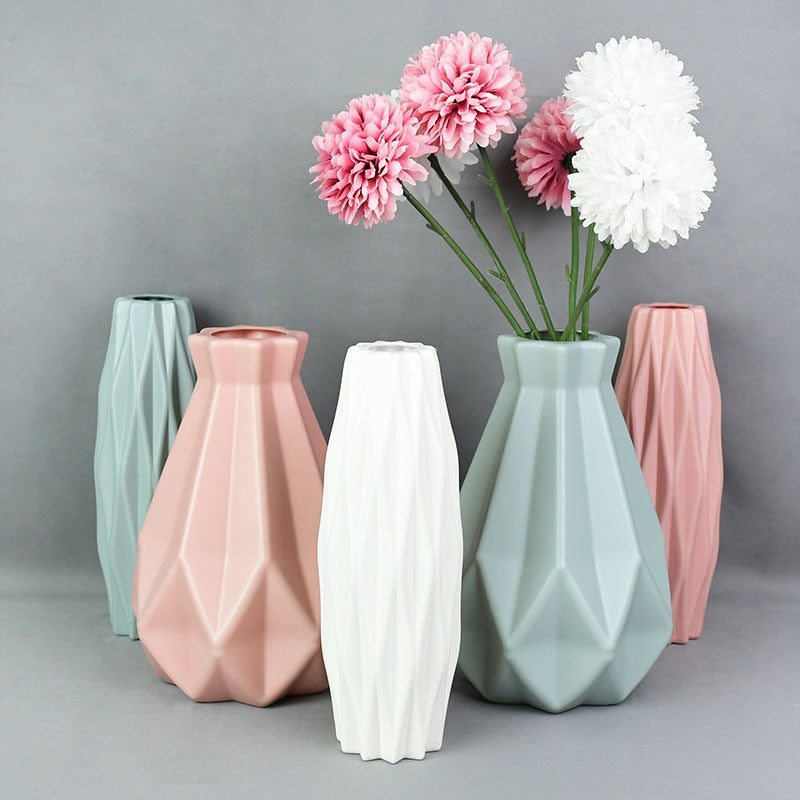 A collection of origami vases in white, pink, and turquoise colors displayed with flowers.