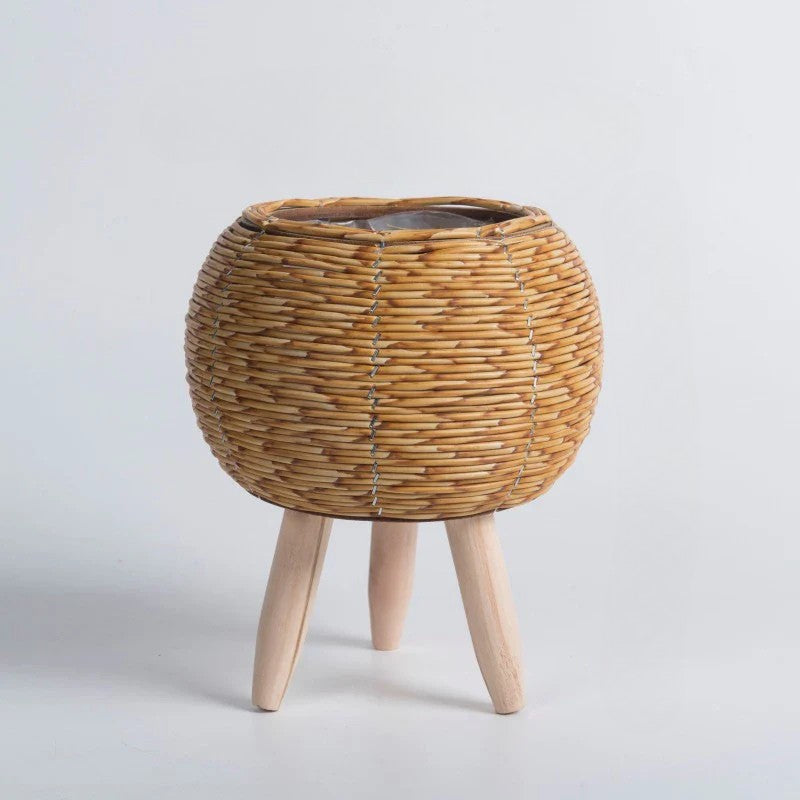 Wicker plant stand with wooden legs on a light gray background