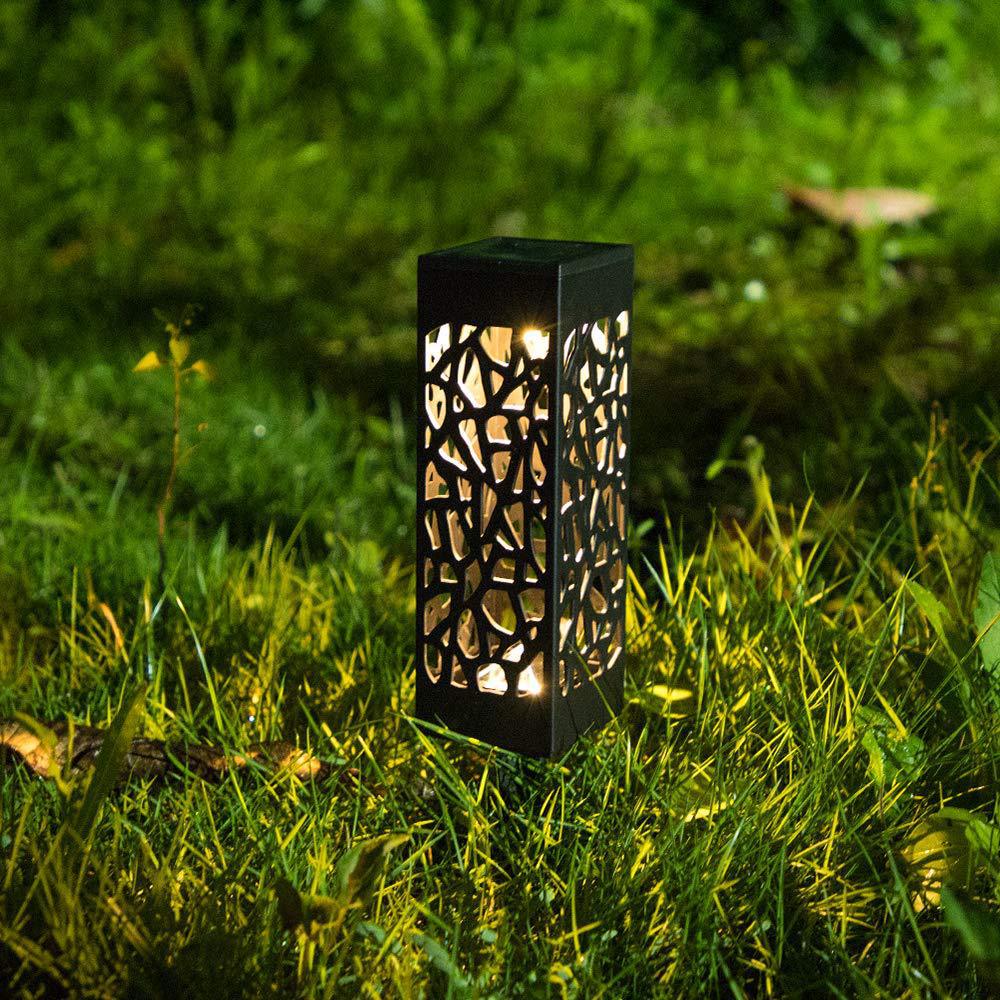 A solar garden path light with a rectangular black frame and intricate cut-out pattern, illuminated and placed on grass.