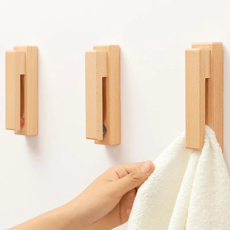 A person hanging a white towel on a wooden towel hook mounted on a white wall.