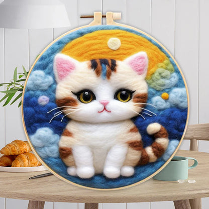 A person's hands holding a DIY felting kit with a pre-printed felt cloth depicting a white cat with orange spots, surrounded by colorful wool in the background.