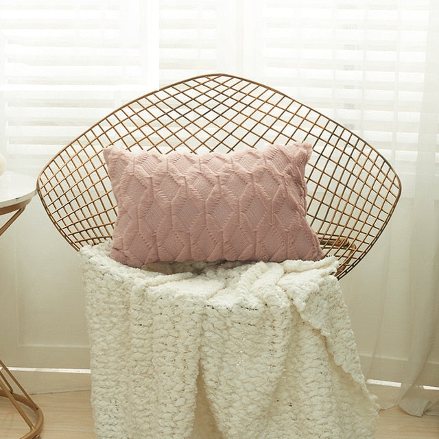 A collection of various colored cushion covers displayed on a wooden stool and the floor, with a few cushions inserted into the covers showcasing a textured design.