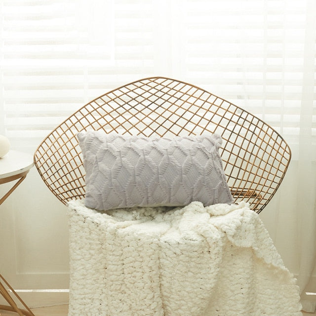 A collection of various colored cushion covers displayed on a wooden stool and the floor, with a few cushions inserted into the covers showcasing a textured design.