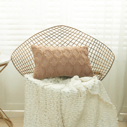 A collection of various colored cushion covers displayed on a wooden stool and the floor, with a few cushions inserted into the covers showcasing a textured design.
