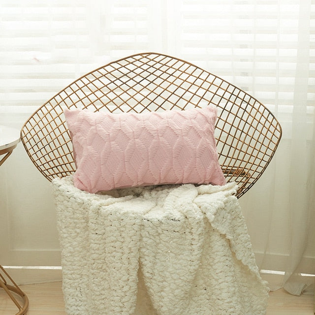 A collection of various colored cushion covers displayed on a wooden stool and the floor, with a few cushions inserted into the covers showcasing a textured design.