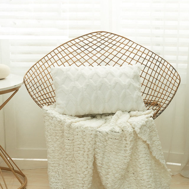 A collection of various colored cushion covers displayed on a wooden stool and the floor, with a few cushions inserted into the covers showcasing a textured design.