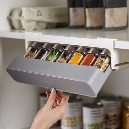 A foldable gray spice bottle holder organizer being mounted under a shelf, with various spice bottles inside.
