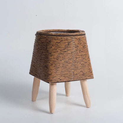 Wicker plant stand with wooden legs on a light gray background
